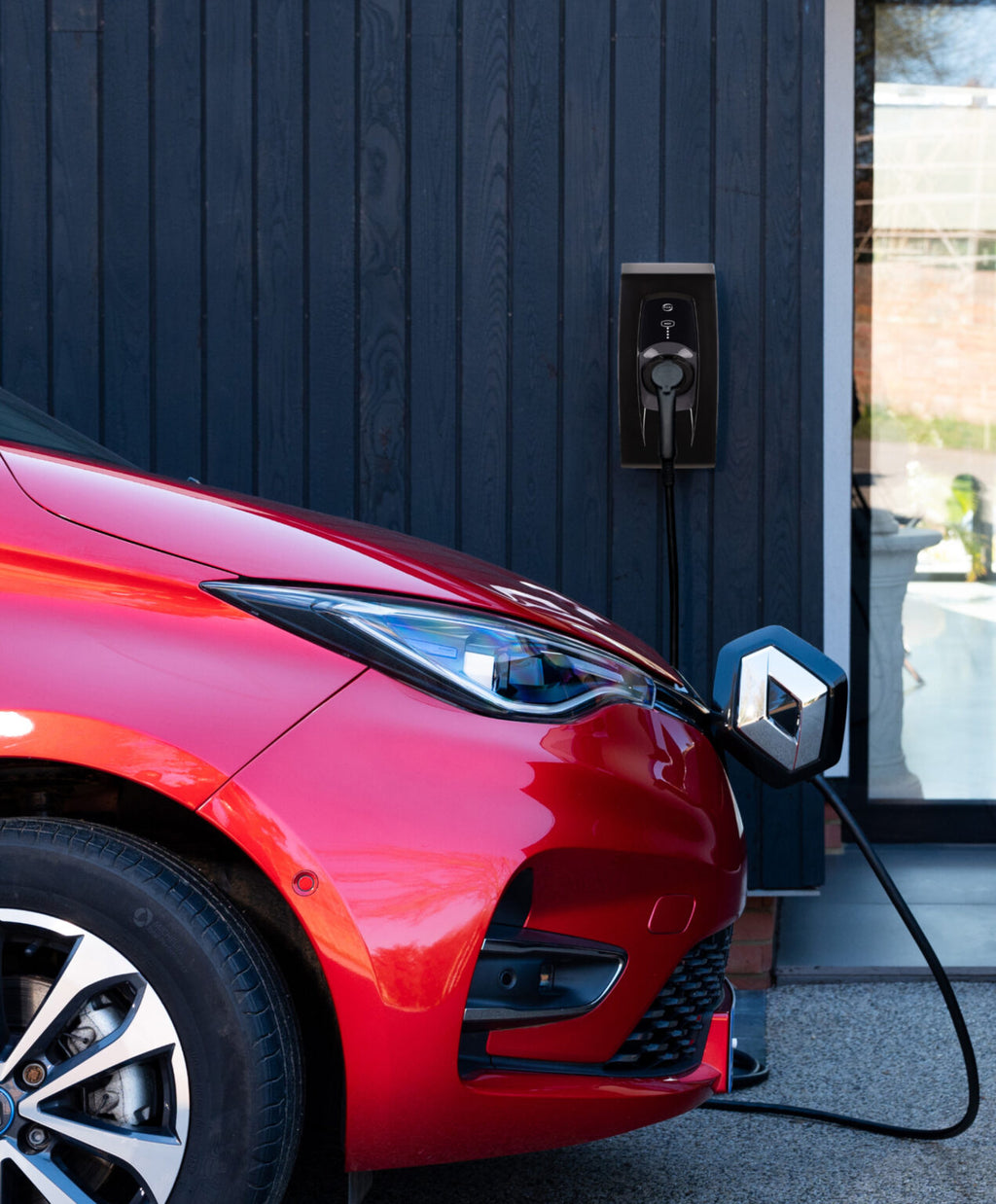 Indra Smart PRO black untethered home EV charger lifestyle install on dark cladded wall with red Renault Zoe plugged in via Renault Type 2 cable