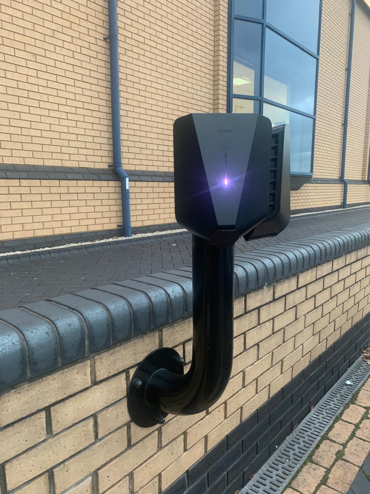 Easee Home EV charger in black installed on wall outdoors with purple LED indicator light illuminated