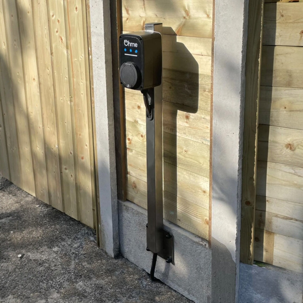 Ohme ePod EV charger installed on pedestal stand against wooden fence in outdoor setting