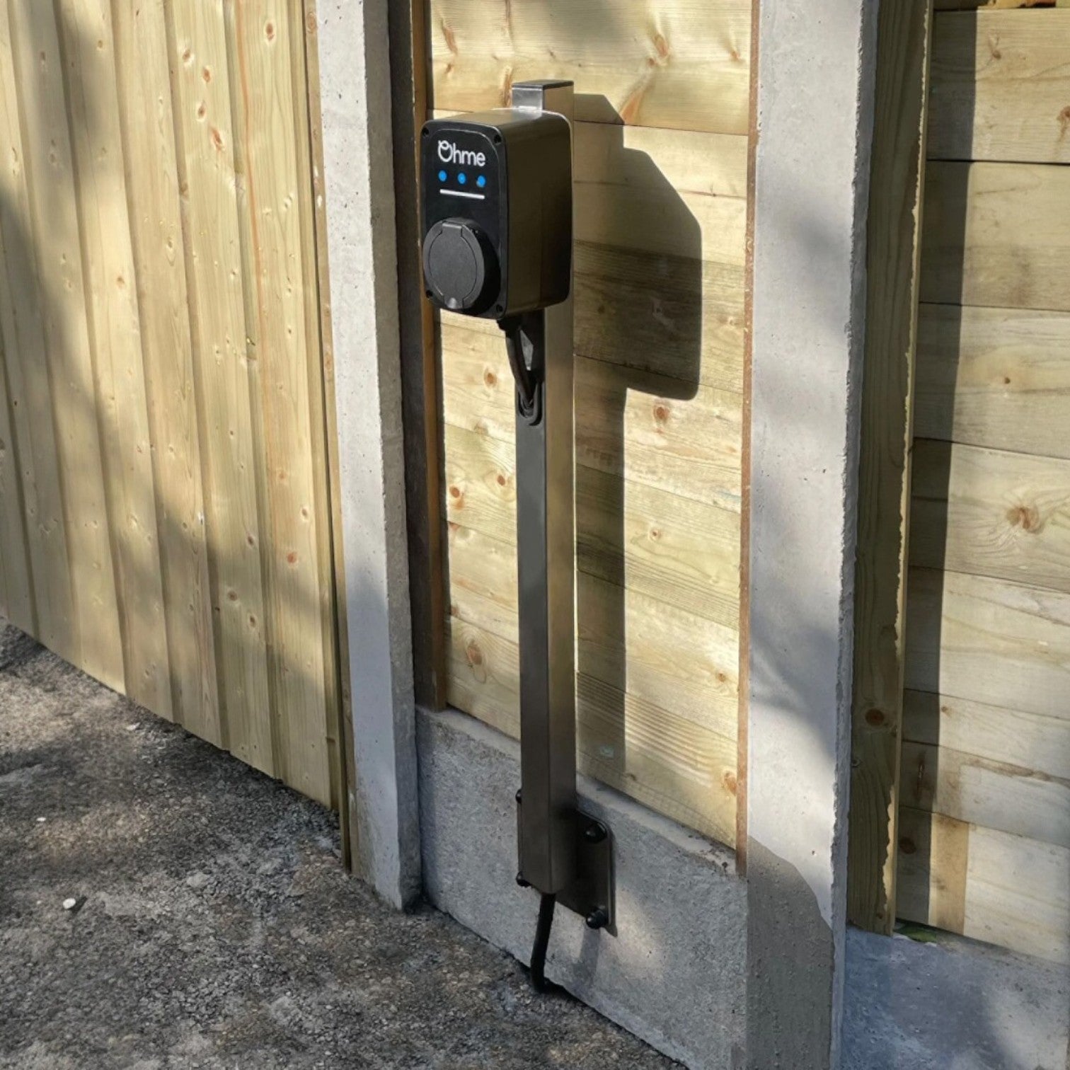 Ohme ePod EV charger installed on pedestal stand against wooden fence in outdoor setting