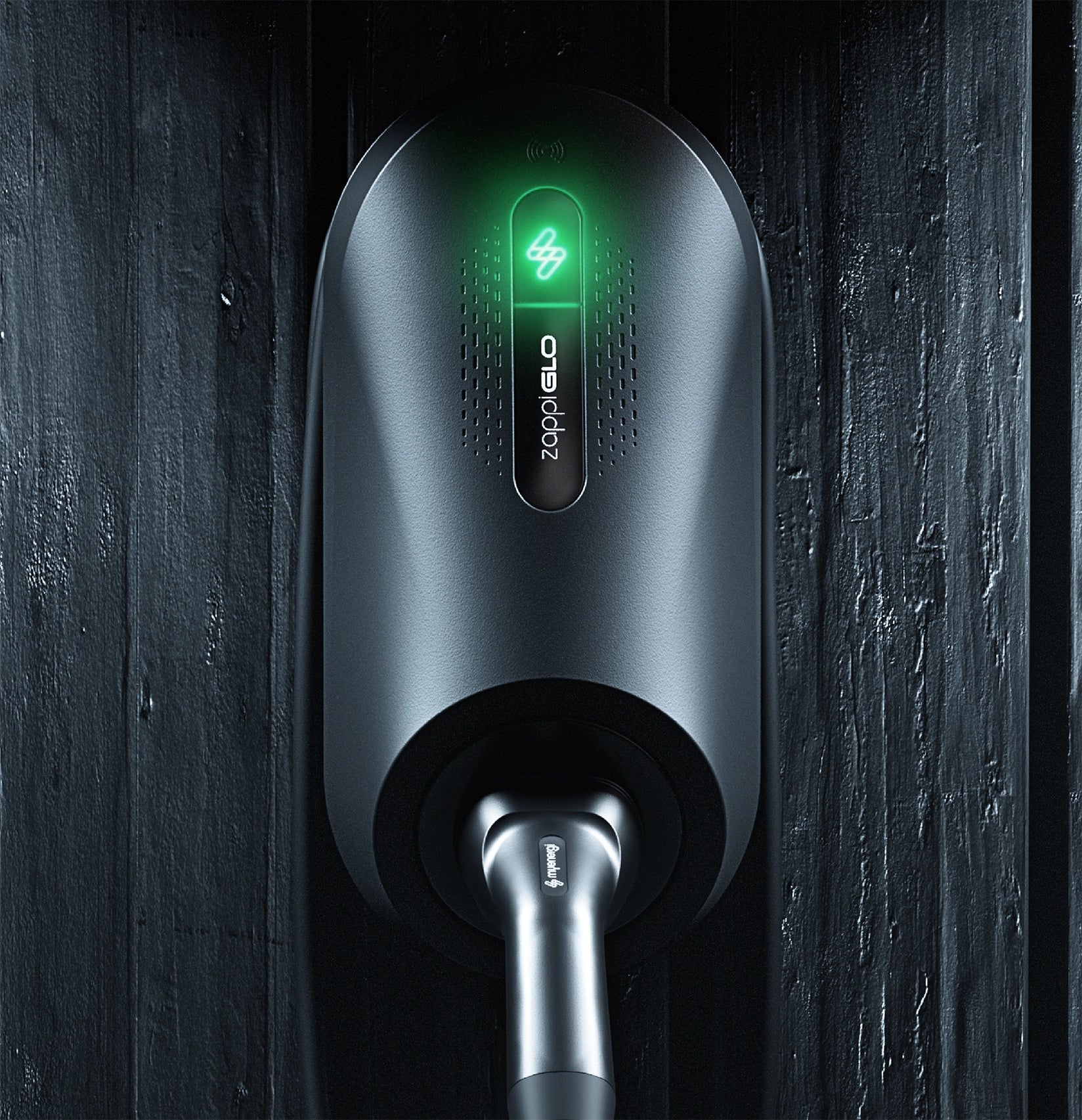 Myenergi Zappi GLO illuminated home EV charger in black mounted on dark wood slat wall with green zappiGLO logo glowing and Type 2 cable plugged in below