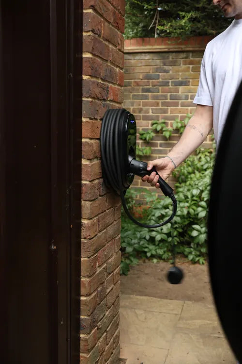 vCHRGD Seven Pro EV charger installed on brick wall, person plugging in cable - UK home charger